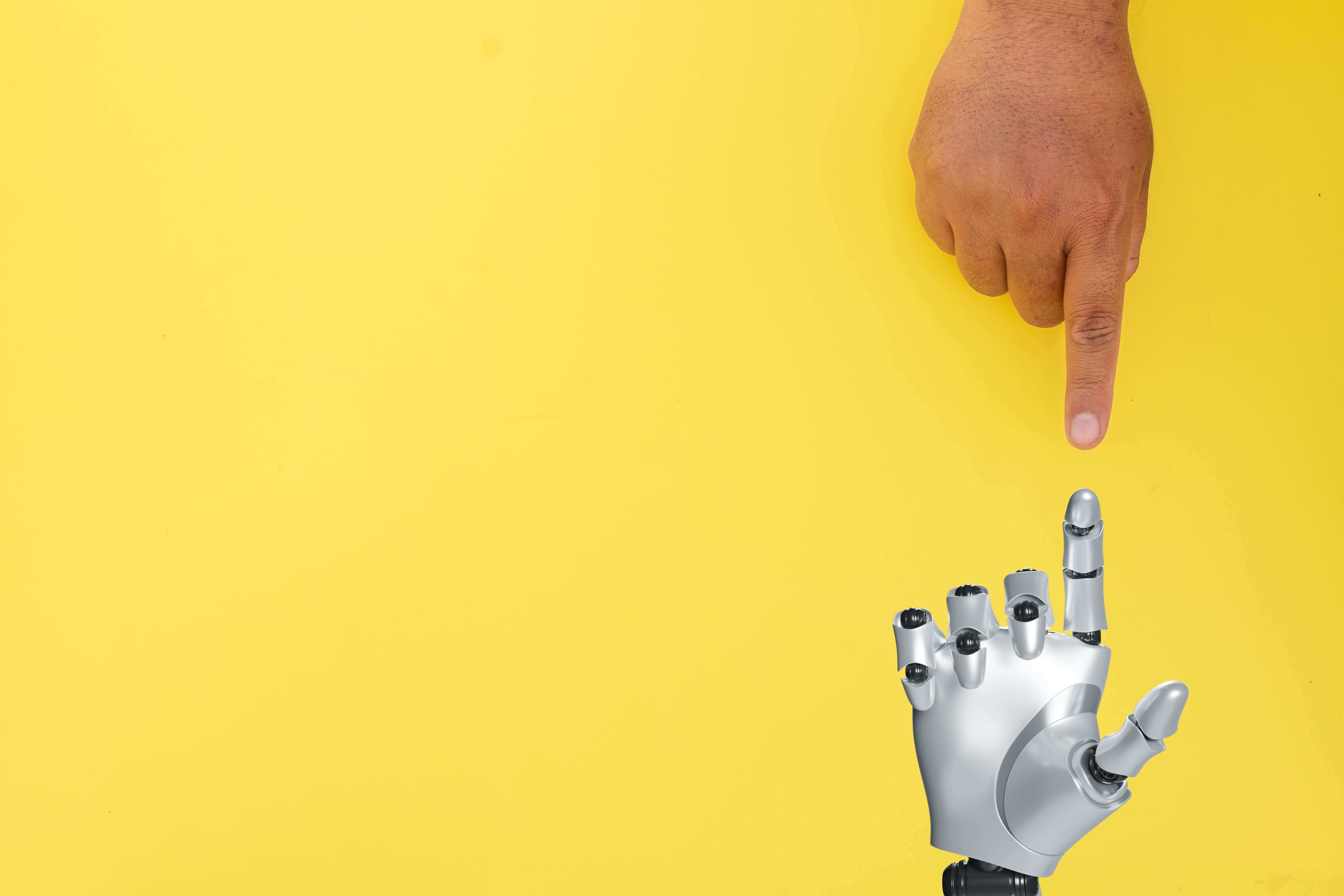 Human,Hand,Touching,Robot,Hand,Over,Yellow,Background,With,Copyspace